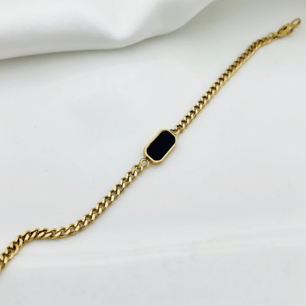A gold chain bracelet featuring a small, rounded rectangular black inlay or stone in the center, displayed on a clean white background.
