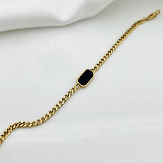 A gold chain bracelet featuring a small, rounded rectangular black inlay or stone in the center, displayed on a clean white background.
