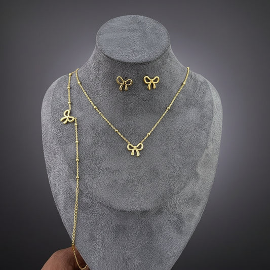 Gold bow-shaped necklace and earrings on a gray mannequin bust.