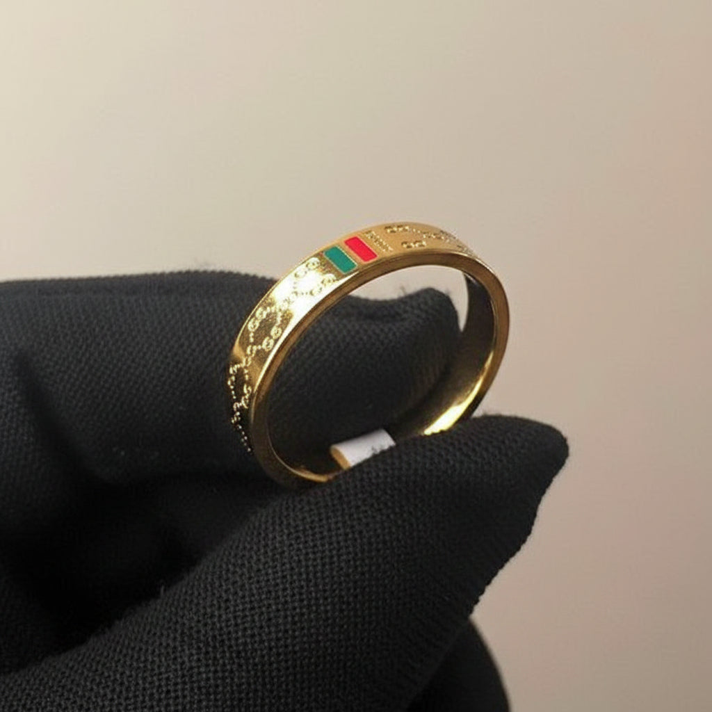Gold ring with engraved design on a black glove against a beige background