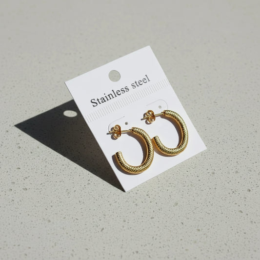 Gold hoop earrings on a white card with 'Stainless steel' text, placed on a gray surface.