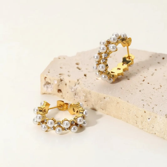 Gold hoop earrings with pearl accents on a beige stone surface