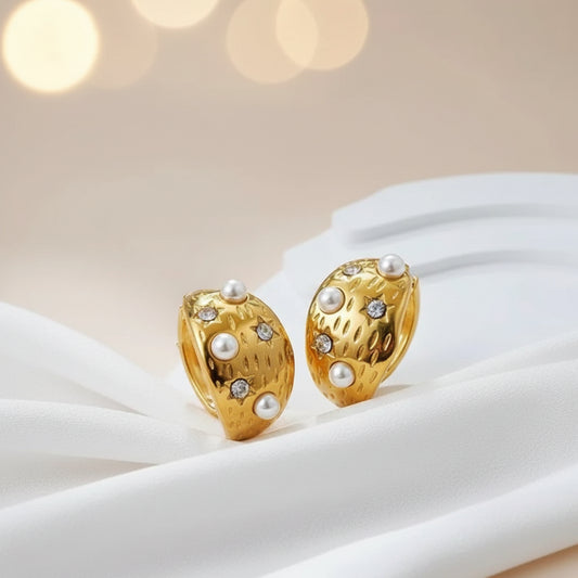 Gold earrings with pearls and gemstones on a white surface