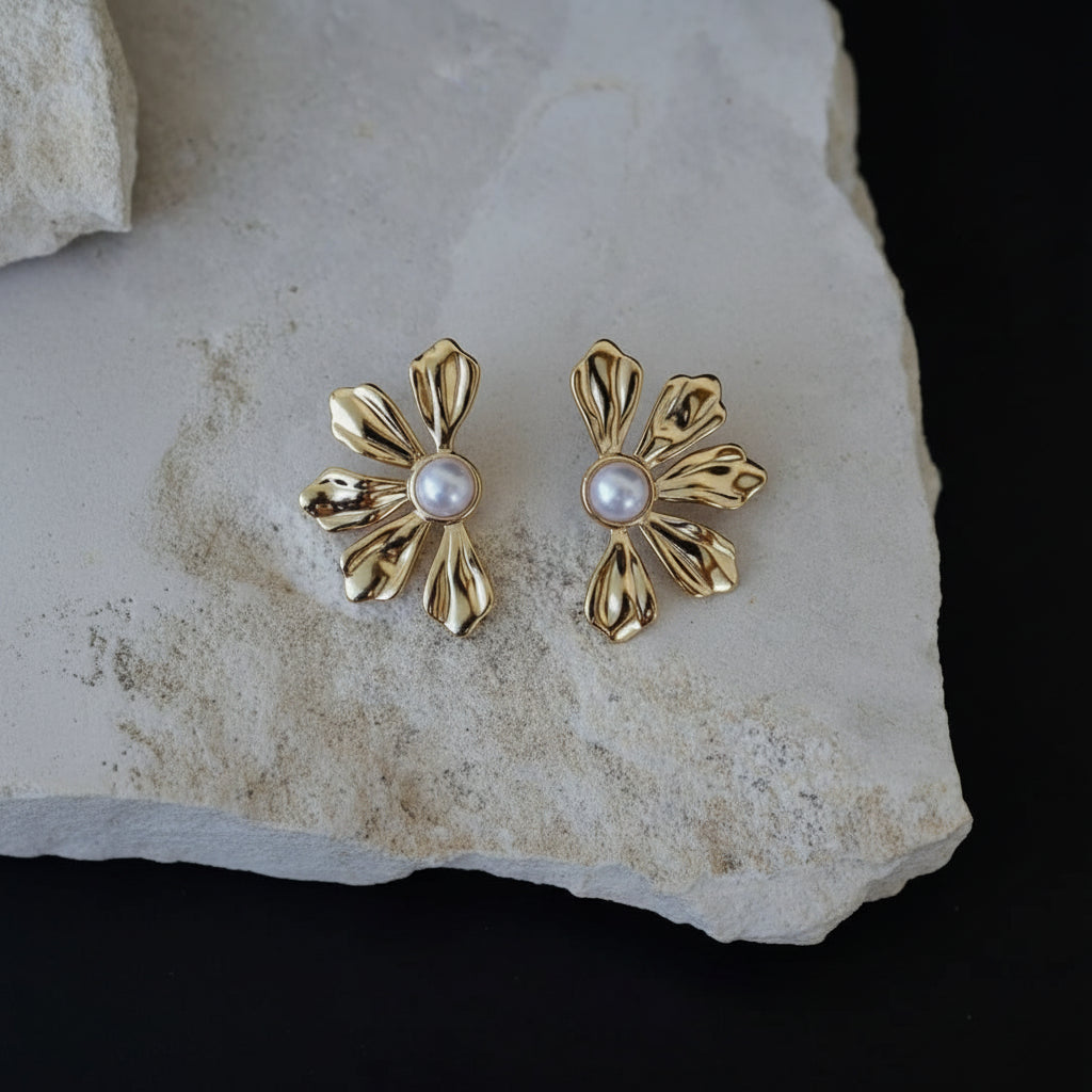 Gold earrings with pearl centers on a stone surface