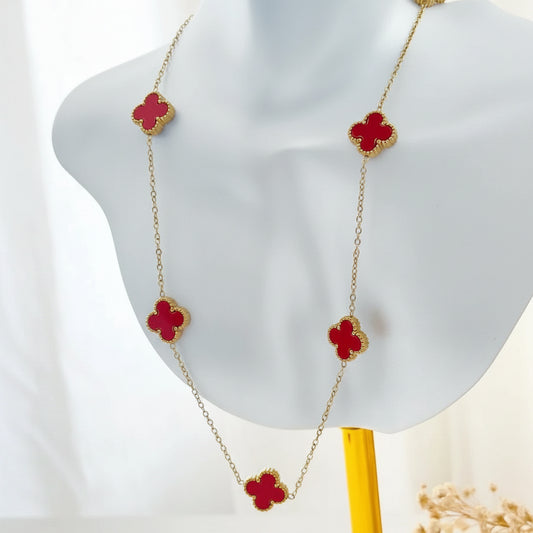 A gold chain necklace with five red clover-shaped charms, displayed on a white mannequin bust.