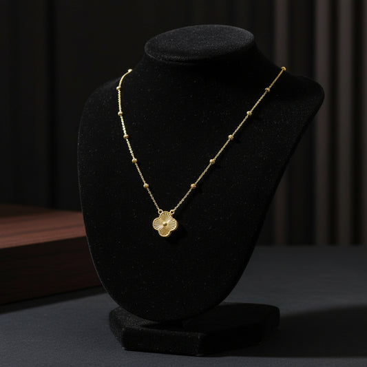 A delicate gold necklace with a textured four-leaf clover pendant, displayed on a white textured jewelry bust.