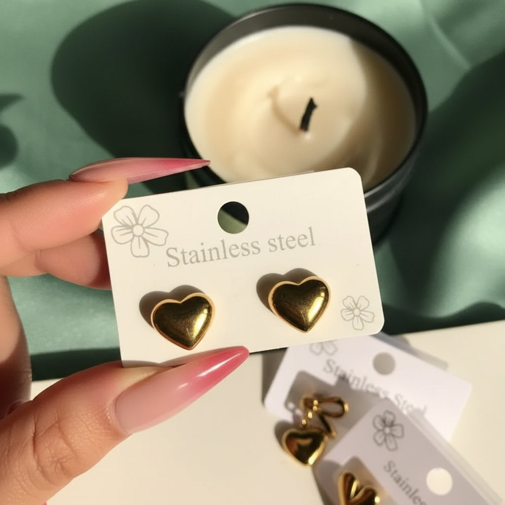 Gold heart-shaped earrings on a 'Stainless Steel' card held by a hand with pink nail polish.