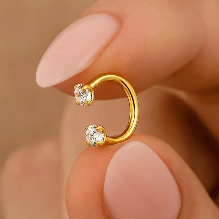 Gold hoop earrings with clear gemstones on a hand against a beige background