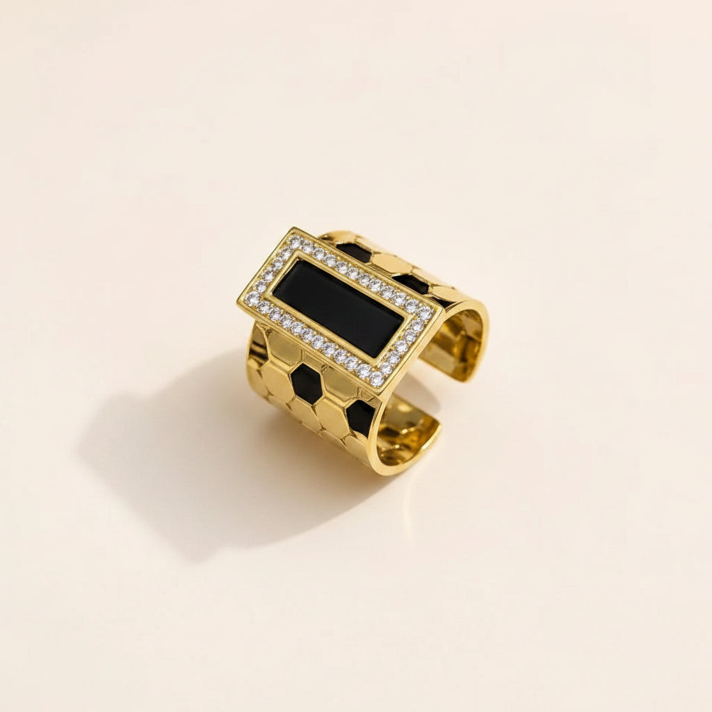 A gold-toned open cuff ring featuring a rectangular black inlay bordered by small clear stones, photographed on a clean off-white background.