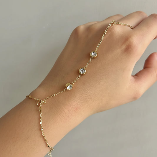 A delicate gold chain anklet with four clear round crystal beads, shown worn on a person's ankle with their hand resting above it, set against a plain light gray background.