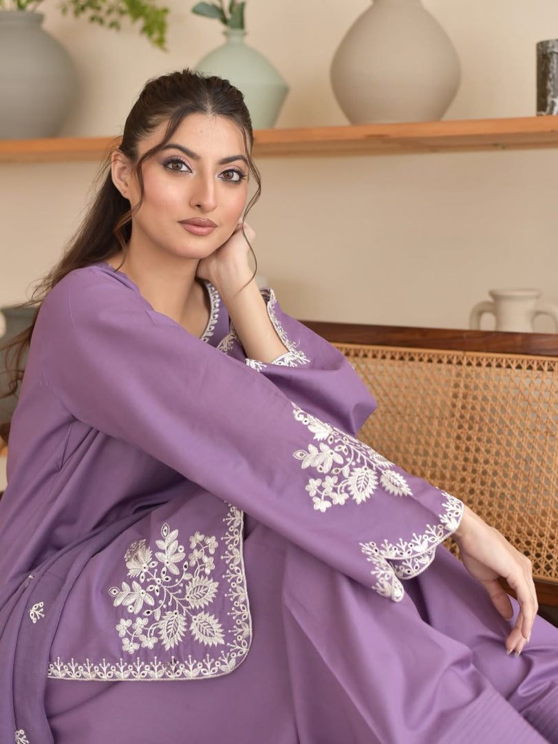 Woman wearing a purple traditional outfit with white embroidery, sitting indoors.
