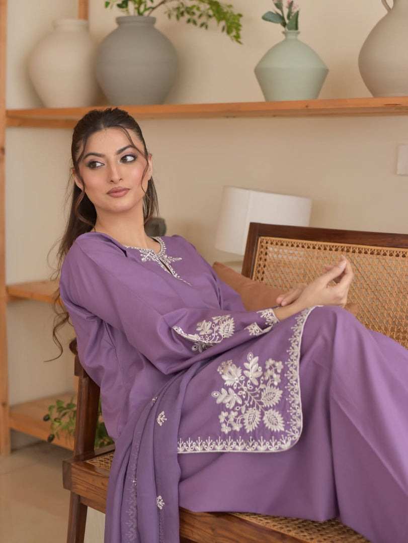 Woman in a purple traditional outfit with white embroidery sitting on a wooden chair.