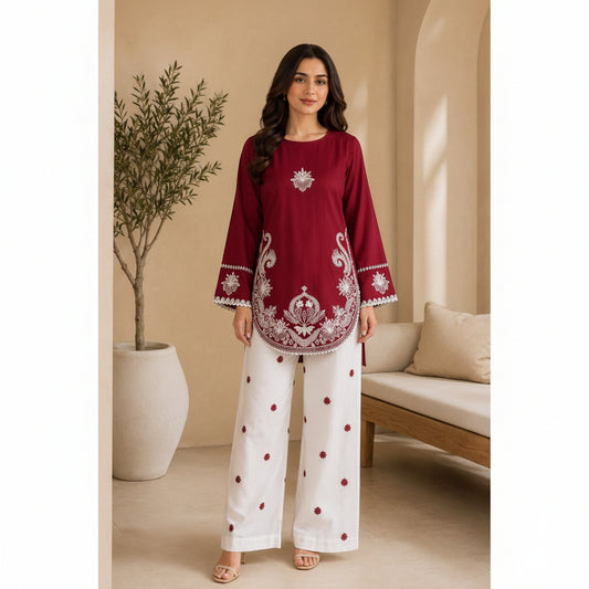 A woman modeling a deep maroon embroidered kurta with white wide-leg pants in a warm, neutral-toned indoor setting.