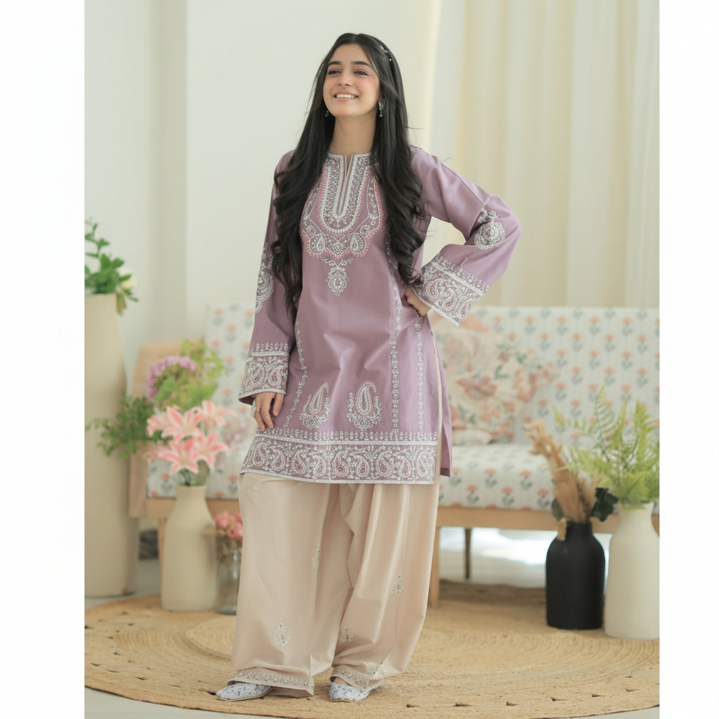 A woman modeling a lavender purple and beige ethnic salwar kameez suit with intricate silver embroidery, standing in a decorated indoor setting with a floral sofa and plants. Text at the bottom reads 'FLAT 20% OFF'.