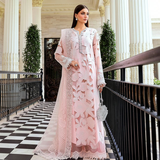A woman models a light pink traditional embroidered dress with a matching sheer lace outer layer in an elegant indoor corridor with black-and-white checkered flooring.