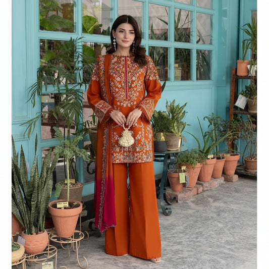 A woman models a traditional South Asian outfit consisting of an orange kurta and matching wide-leg trousers with a matching dupatta. The outfit features intricate white floral embroidery and a vibrant magenta gradient at the bottom of the dupatta.