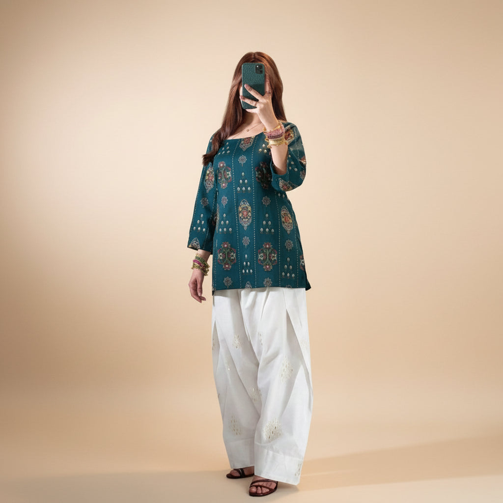 Person wearing a dark blue patterned top and white pants against a plain wall.