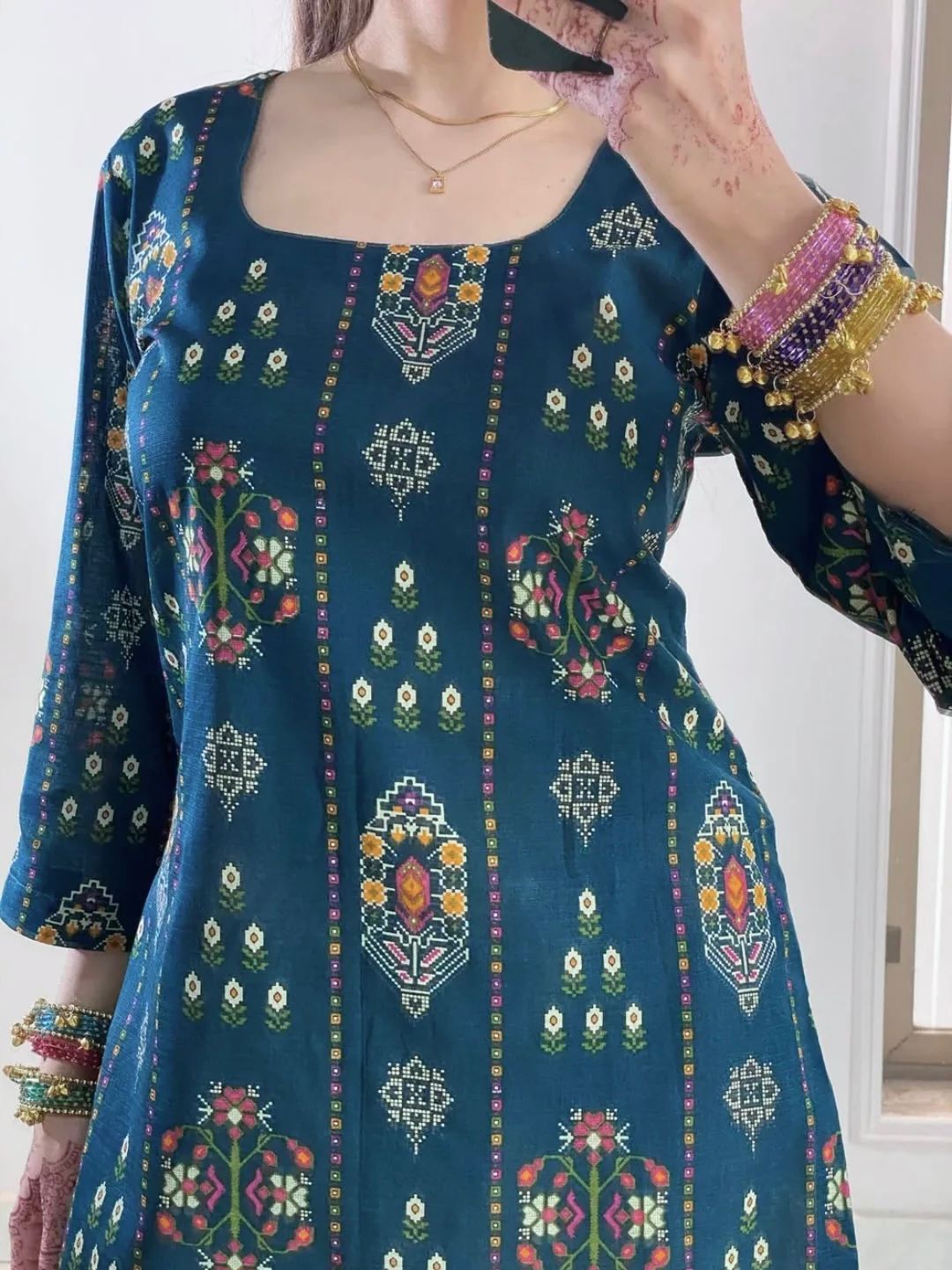 Blue embroidered traditional outfit with colorful patterns and jewelry.