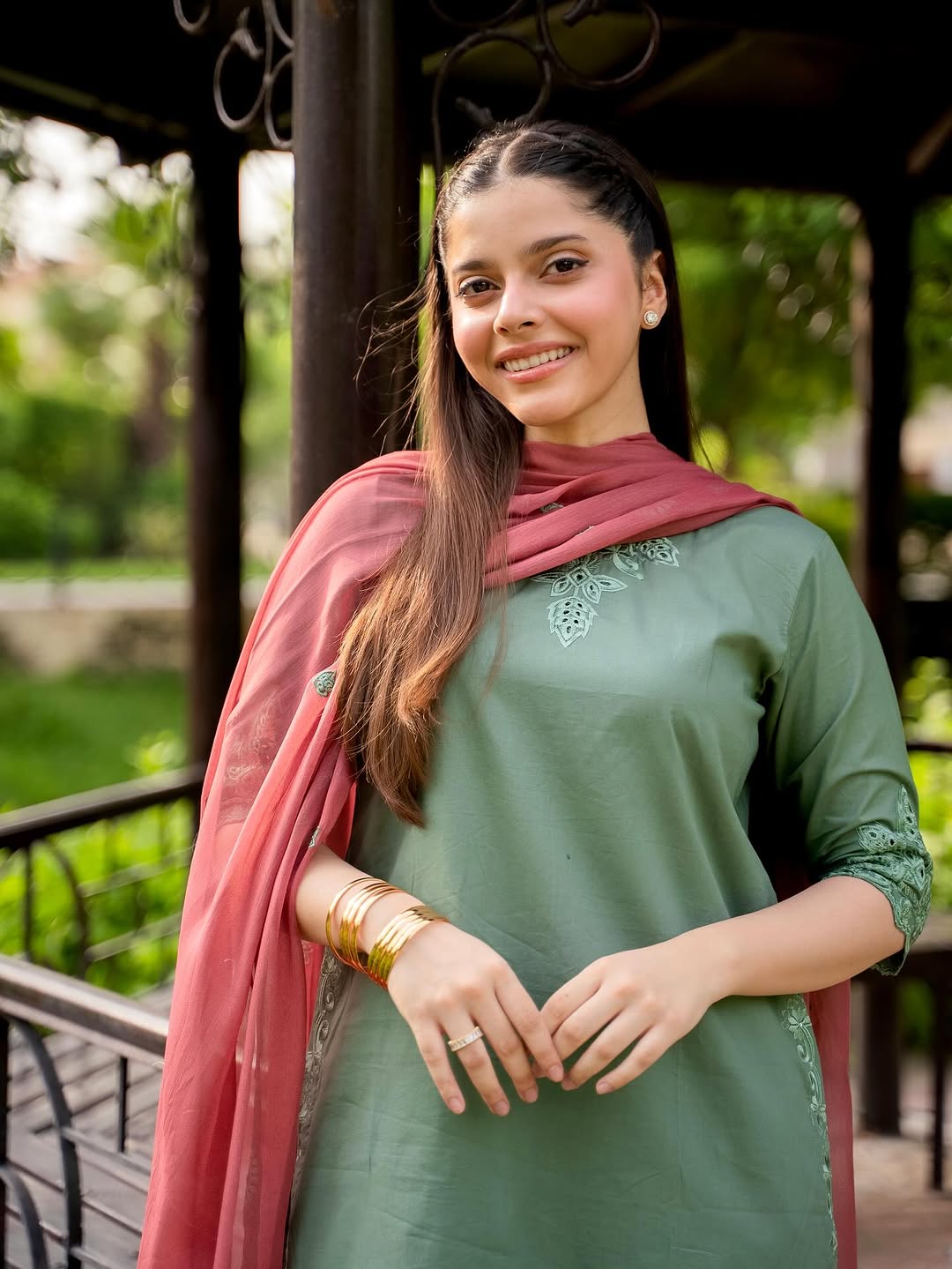Woman wearing a green outfit with a pink dupatta in an outdoor setting