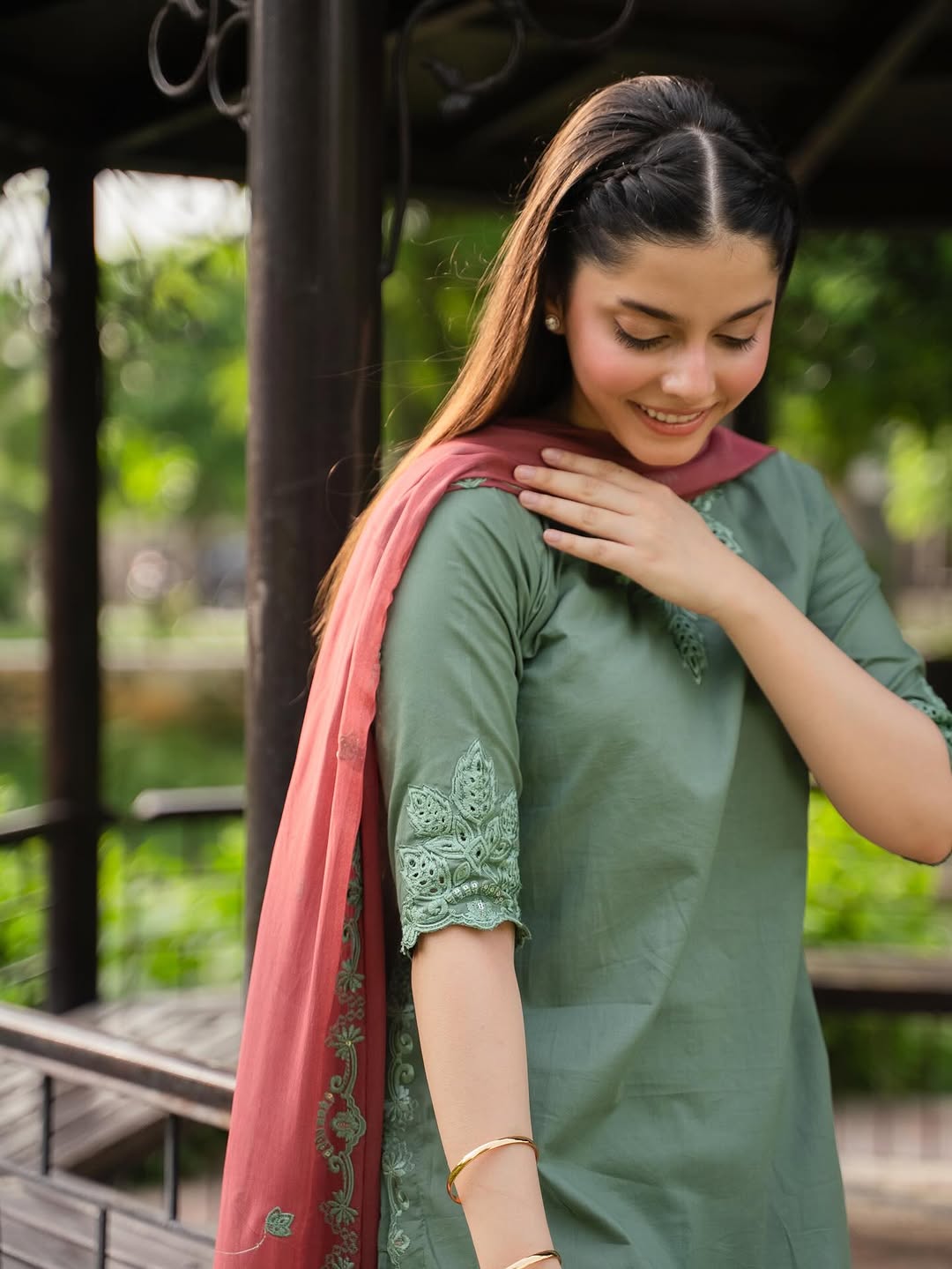 Woman in a green traditional outfit with a pink dupatta, standing outdoors.