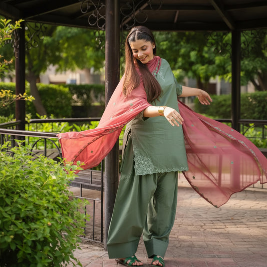 Woman in green traditional outfit with pink dupatta standing outdoors