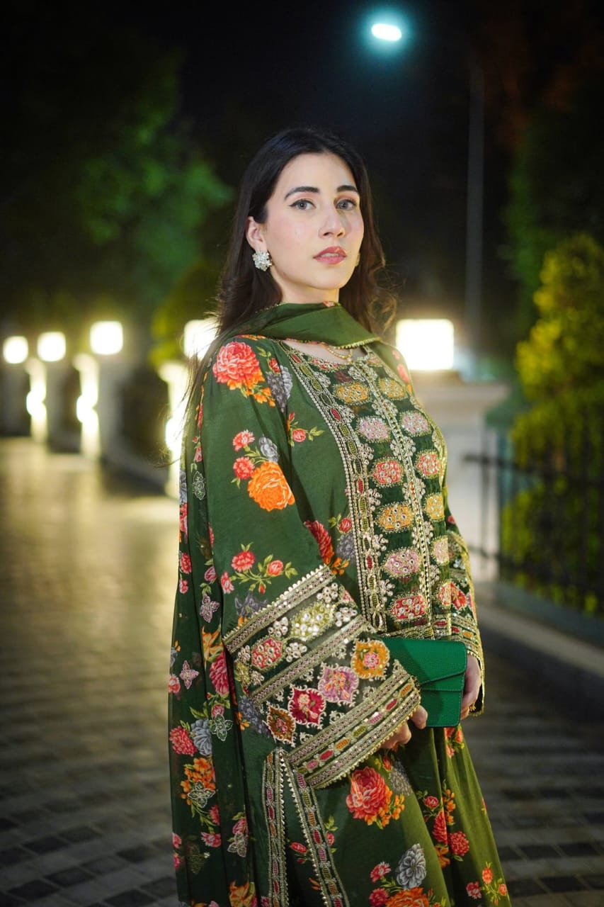 Woman in a green embroidered traditional outfit standing on a pathway at night.