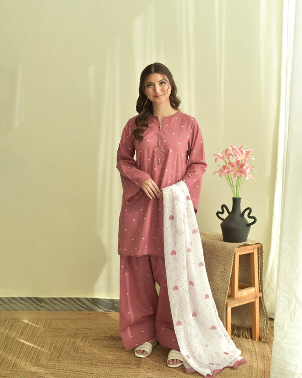 Woman in a pink traditional outfit with a white scarf in a room with a vase and flowers.