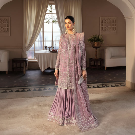 Woman in a pink embroidered traditional outfit standing in a room with decor elements.