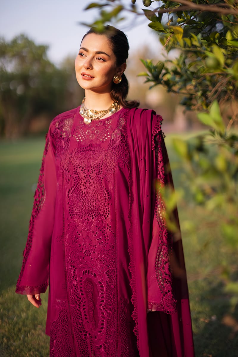 Woman in a magenta traditional outfit standing outdoors with greenery in the background