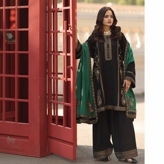 A woman modeling a black three-piece traditional outfit with gold embroidery and a green dupatta, standing next to a red telephone booth.
