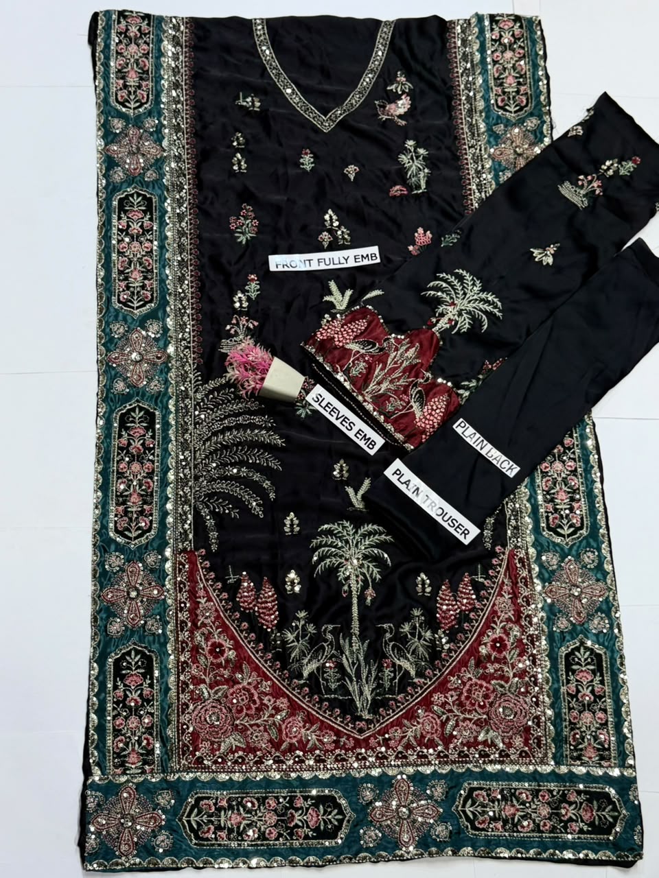 Black 3-piece salwar suit fabric set with intricate multicolor embroidery, featuring a kurta, pants, and a matching border scarf laid flat on a white background.
