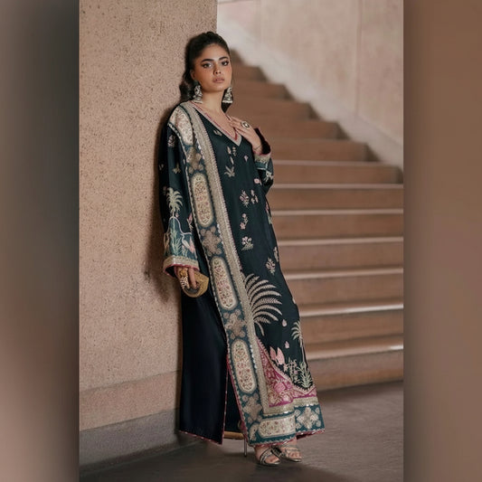 A woman models a dark teal embroidered kurta with beige, pink, and green floral patterns, leaning against a textured wall next to a staircase.