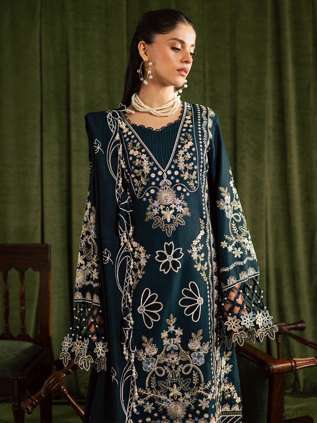 Woman wearing a dark blue embroidered traditional outfit against a green curtain background