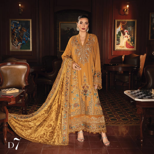 A woman models a traditional long kurta set in a warm golden yellow color with intricate multicolor embroidery, set against a dark wood-paneled room.