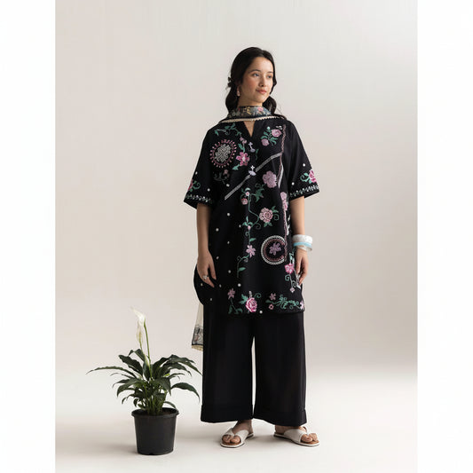 Woman wearing a black embroidered dress with wide-leg pants against a white background