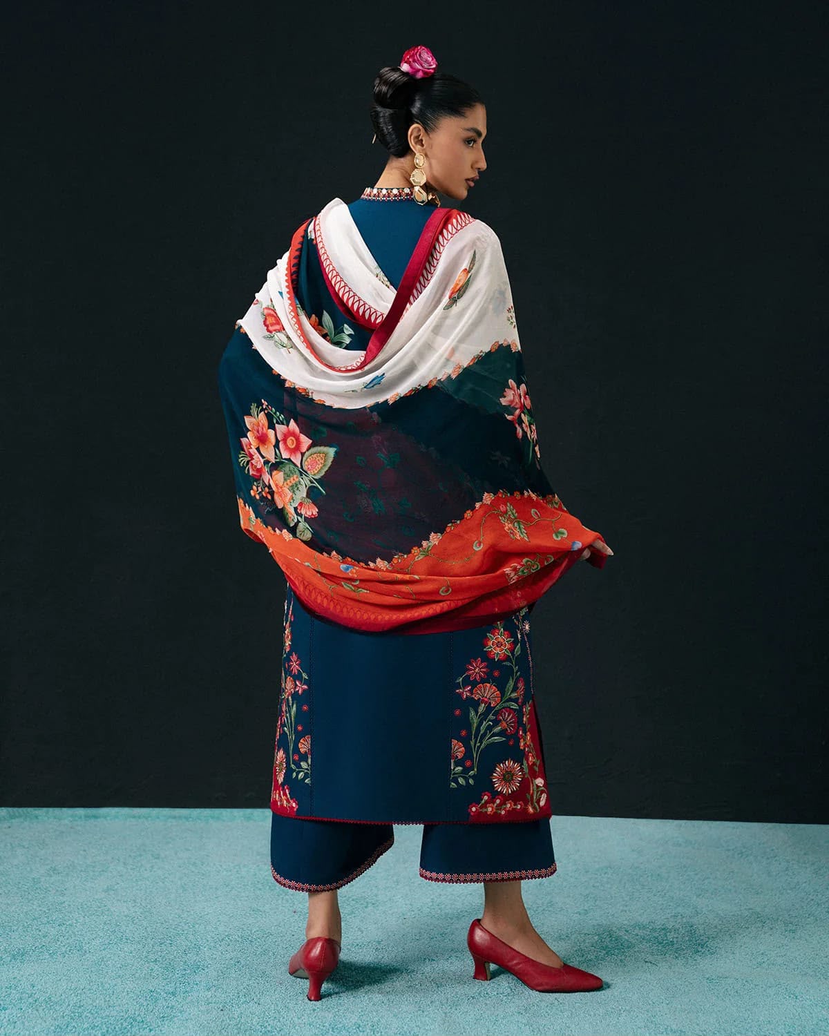 Woman wearing a traditional embroidered outfit with a colorful shawl against a black background