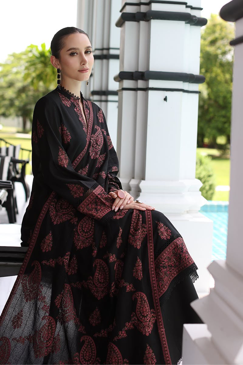 Woman in a black and red patterned dress sitting outdoors with columns and greenery in the background