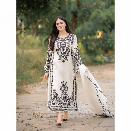Woman wearing a white dress with black embroidery standing outdoors.