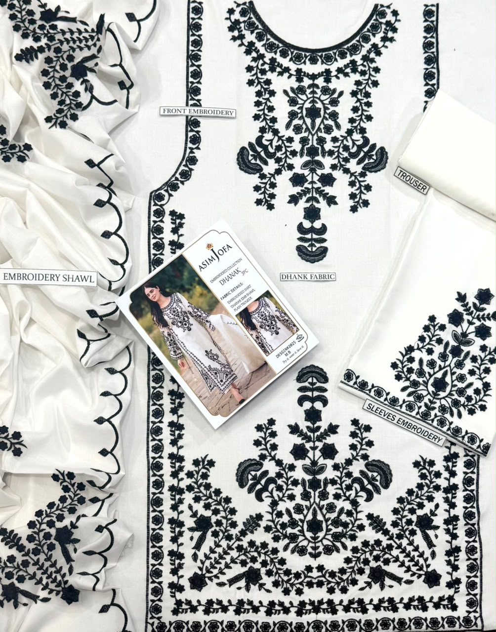 A white embroidered tunic top with black floral and ornamental embroidery, shown in a styled flat-lay with matching fabric pieces and a printed brand card. Visible text includes 'Embroidery Shawl', 'Blouse Fabrics', and 'Saffi Fair'.