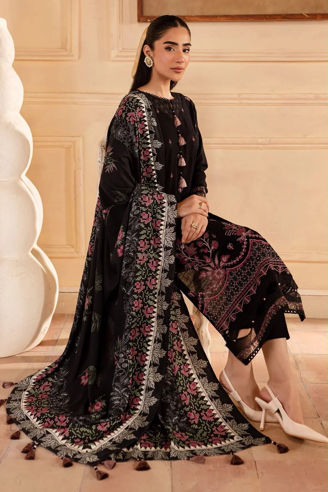 Woman in a black embroidered outfit with floral patterns in an elegant indoor setting.
