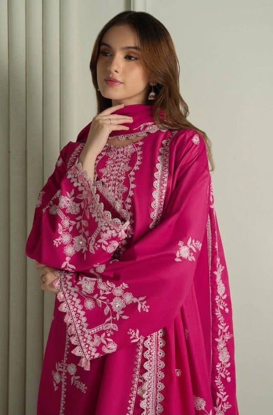 A woman wearing a bright magenta pink traditional outfit with intricate white floral embroidery, standing against a neutral light gray background.