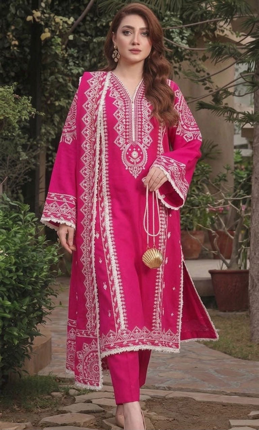 A woman wearing a bright pink traditional outfit with intricate white embroidery, standing outdoors on a stone path with greenery in the background.