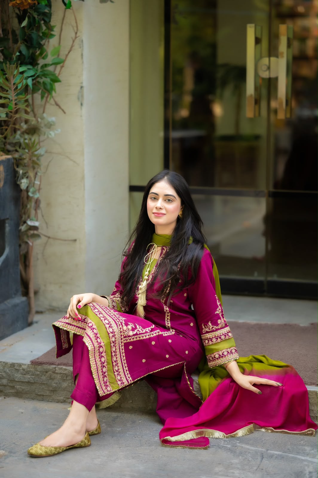 Woman in a traditional pink and green outfit sitting on a stone step.