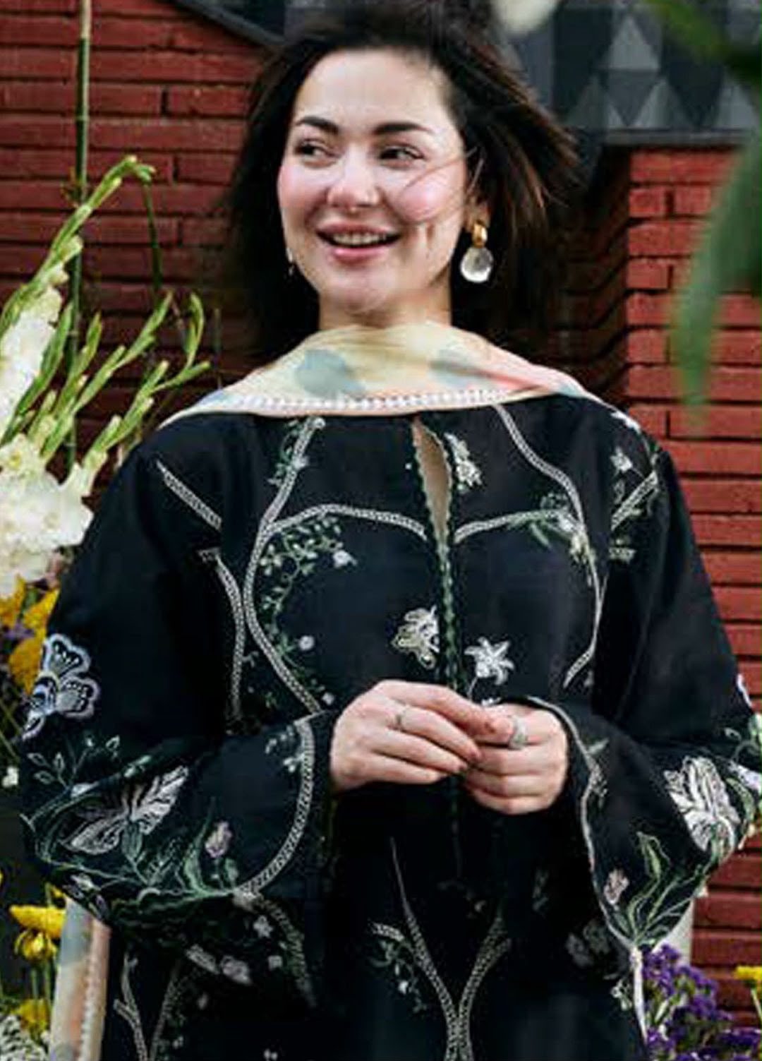 Woman wearing a black embroidered dress with flowers and leaves, standing outdoors.