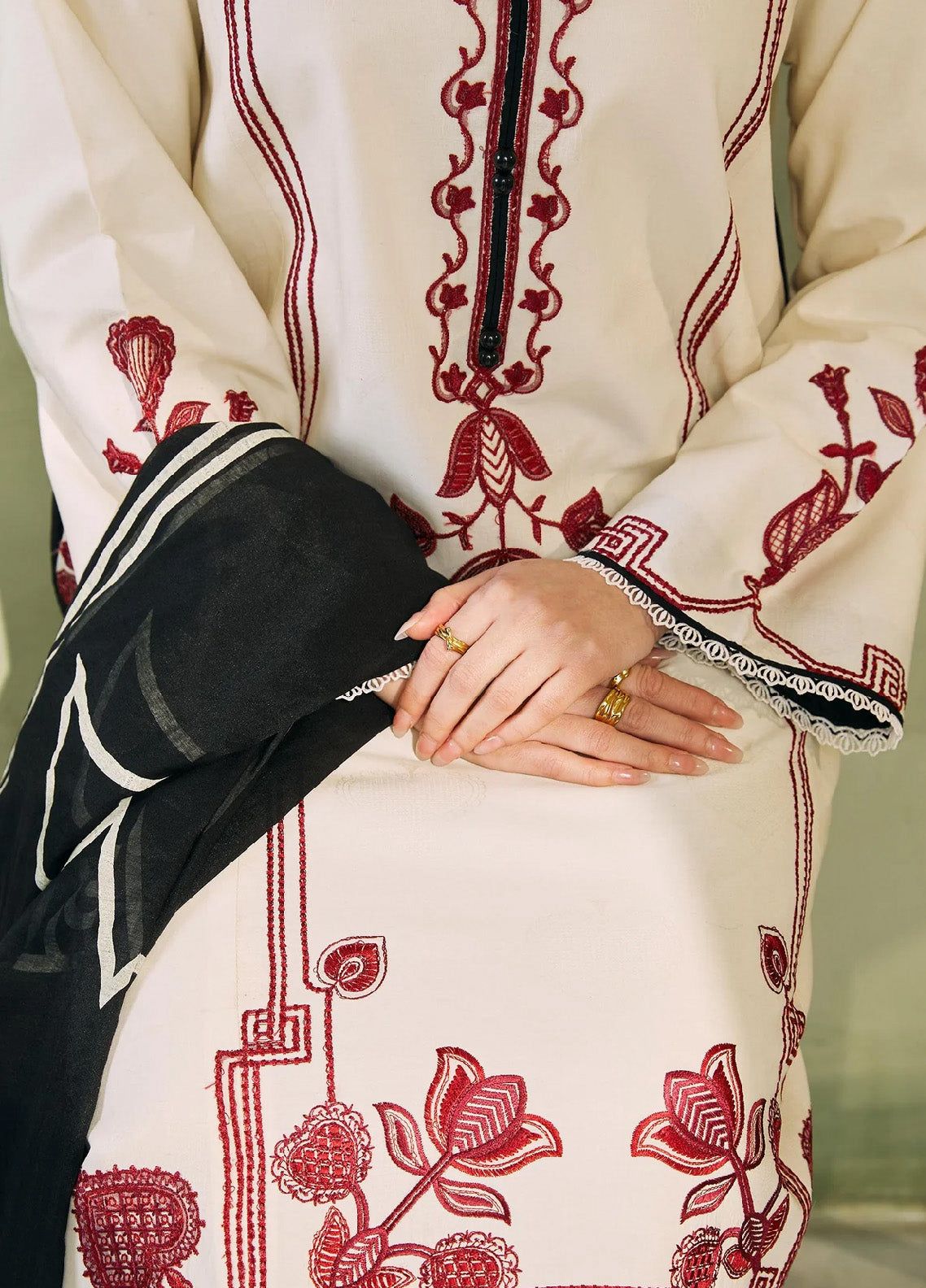 Close-up of a person wearing a cream-colored outfit with red floral embroidery and black accents.