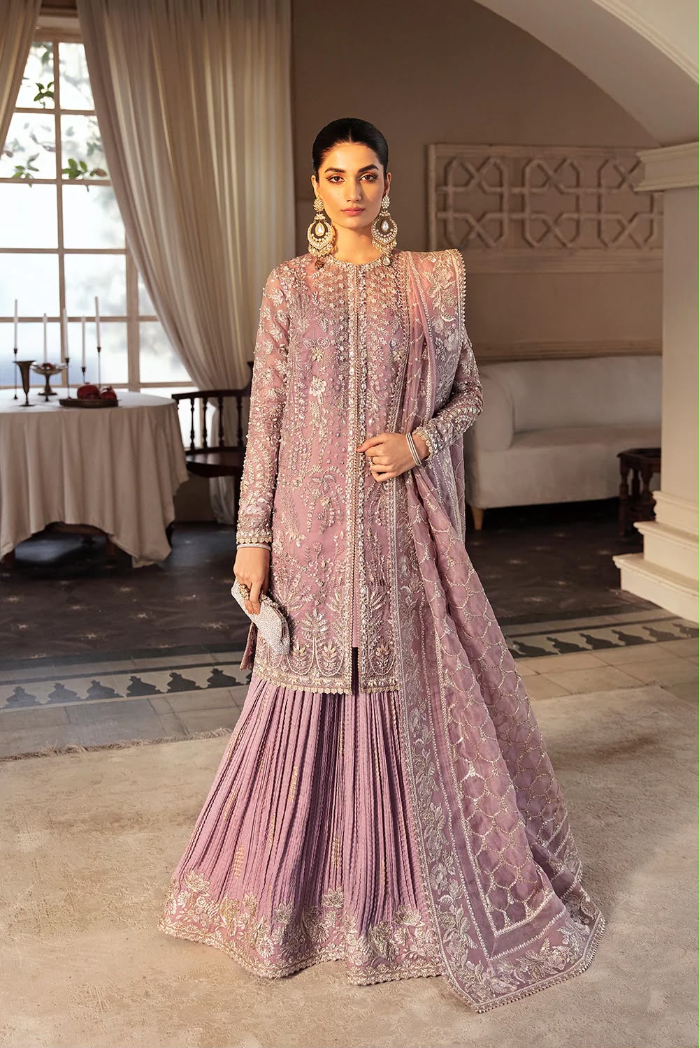 Woman in a pink embroidered traditional outfit standing in an elegant room.