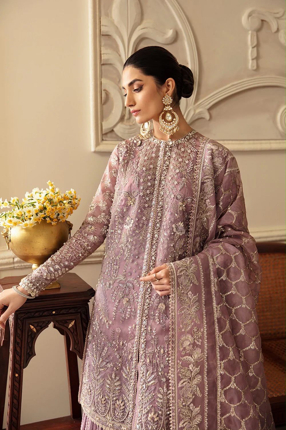 Woman in a lavender embroidered traditional outfit standing in an elegant room.