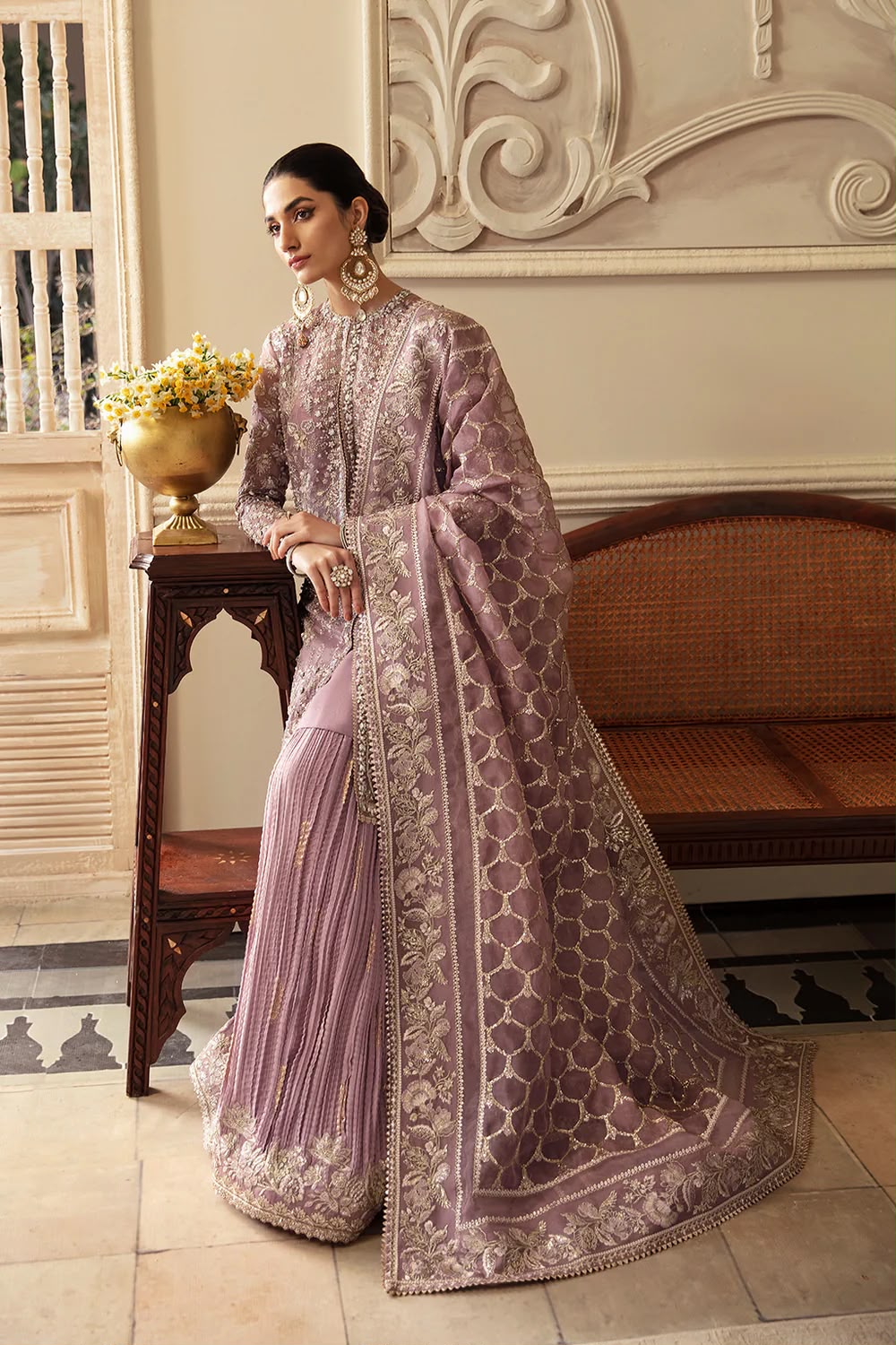 Woman in a traditional lavender saree with intricate patterns in an elegant interior setting.