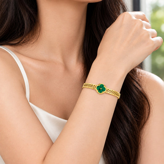 A gold bangle bracelet featuring a central green four-leaf clover motif with a small gold dot in the center, set against a plain white background.