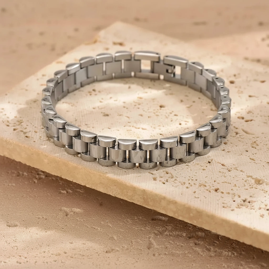 A silver stainless steel link bracelet displayed on a textured beige stone slab.